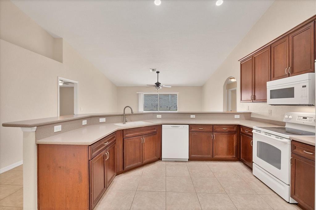 A kitchen with wood cabinets, white appliances, and a breakfast bar overlooking a living area — 15117 LYNEBURG AVENUE, PORT CHARLOTTE, FL