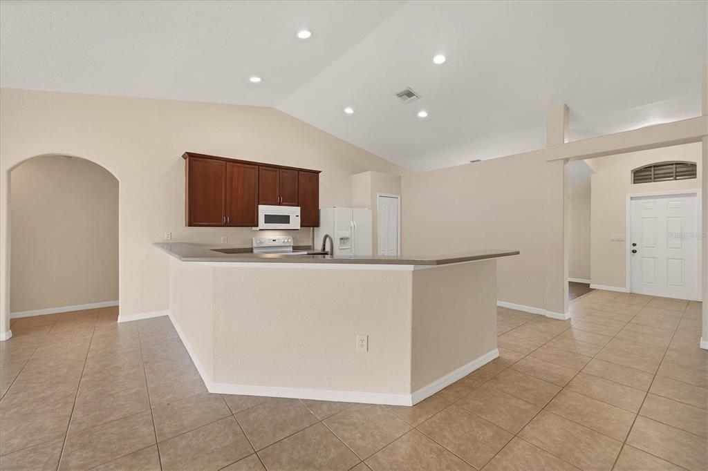 A kitchen with dark wood cabinets and a breakfast bar overlooks an open living area — 15117 LYNEBURG AVENUE, PORT CHARLOTTE, FL