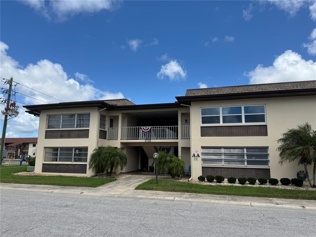 A two-story apartment building exterior with beige walls, brown trim, and a central walkway — 5132 AMULET DRIVE UNIT 101, NEW PORT RICHEY, FL