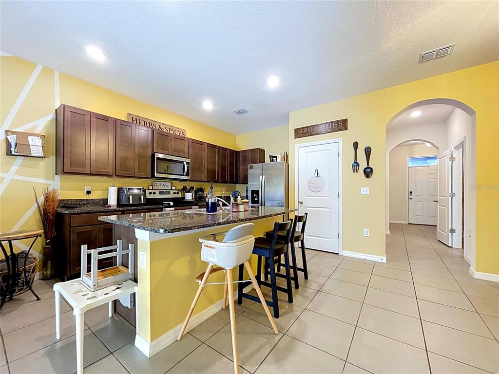 A kitchen features dark wood cabinets, a granite island with seating, and yellow walls — 3221 PLEASANT WILLOW COURT, BRANDON, FL