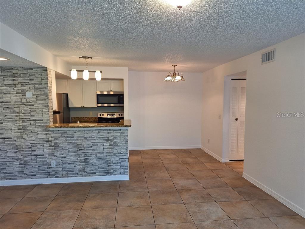 A dining area with tile floors, a chandelier, and a kitchen with a stone-accented bar — 5116 CONROY ROAD UNIT 12, ORLANDO, FL