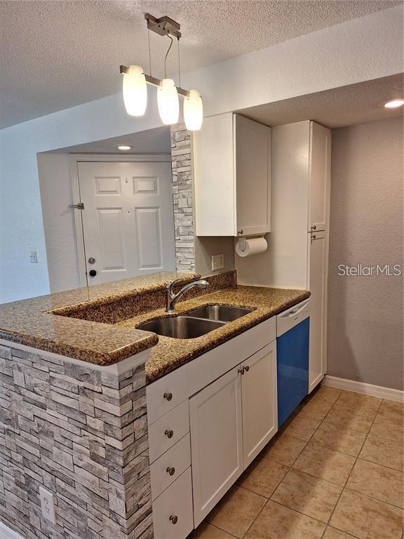 A kitchen features white cabinets, granite countertops, a stone-tiled peninsula, and a blue dishwasher — 5116 CONROY ROAD UNIT 12, ORLANDO, FL