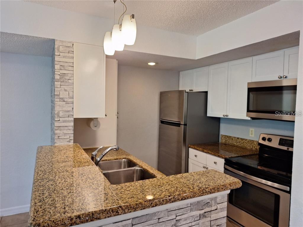 A kitchen features granite countertops, white cabinets, stainless steel appliances, and a stone-accented breakfast bar — 5116 CONROY ROAD UNIT 12, ORLANDO, FL
