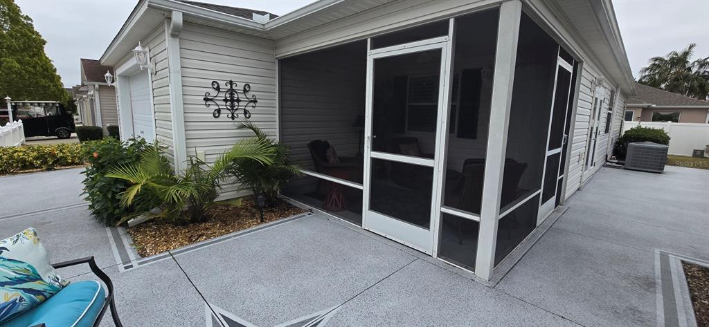 A screened-in patio with a concrete floor sits beside a house with light-colored siding — 1846 KANE PLACE, THE VILLAGES, FL