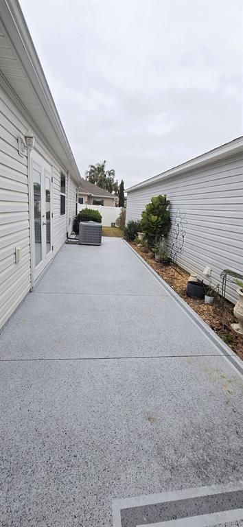 A narrow concrete patio with a speckled finish sits between two light-colored vinyl-sided houses — 1846 KANE PLACE, THE VILLAGES, FL