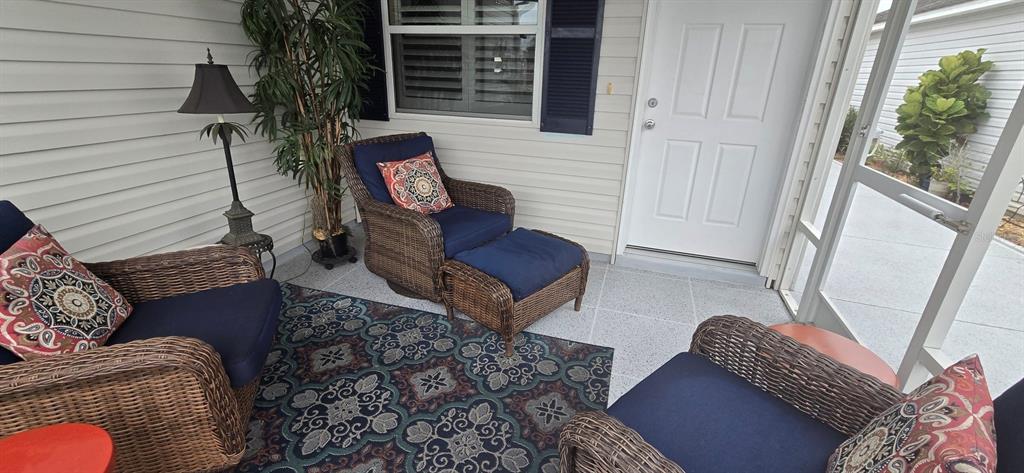 A screened-in porch features wicker furniture with blue cushions, patterned pillows, and a patterned rug — 1846 KANE PLACE, THE VILLAGES, FL