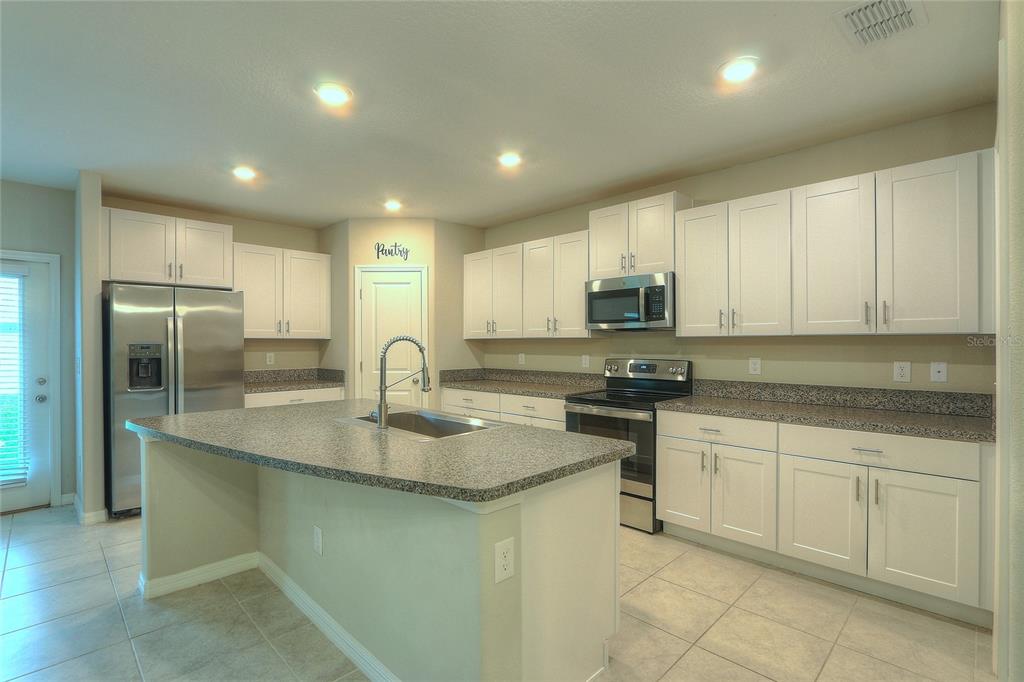 A kitchen with white cabinets, granite countertops, a center island, and stainless steel appliances — 7217 RONNIE GARDENS COURT, TAMPA, FL