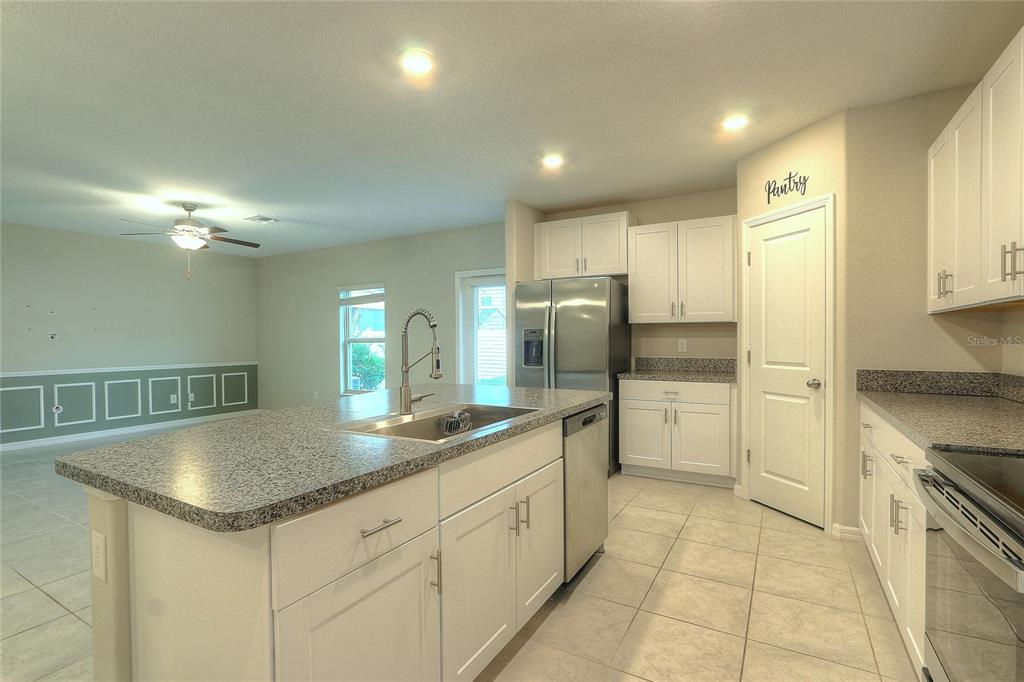 A kitchen features white cabinets, granite countertops, a center island with a sink, and tile flooring — 7217 RONNIE GARDENS COURT, TAMPA, FL