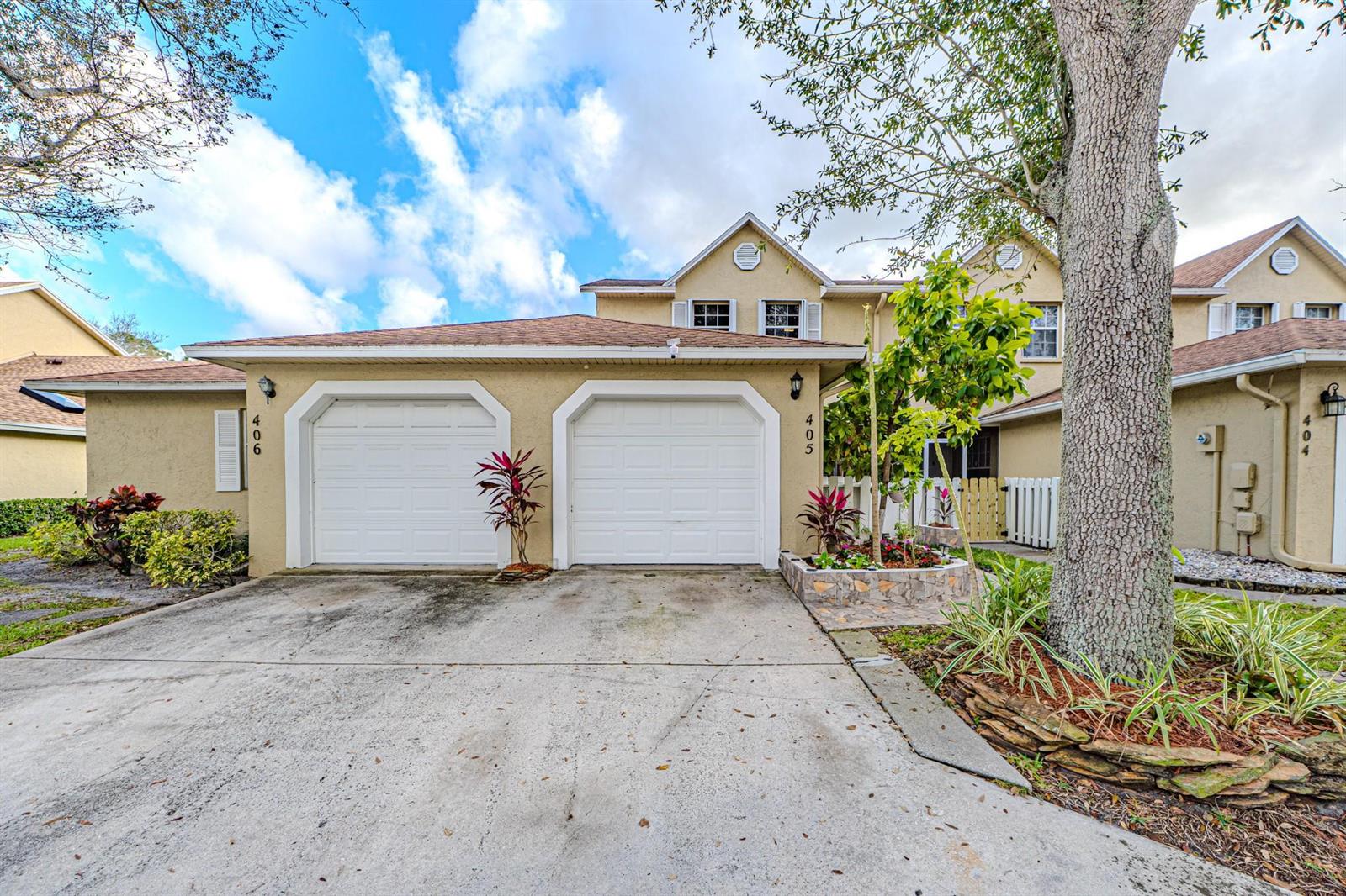 A two-car garage exterior with a concrete driveway and a large tree in front — 405 Maplewood Drive # 405, FL 33415, FL