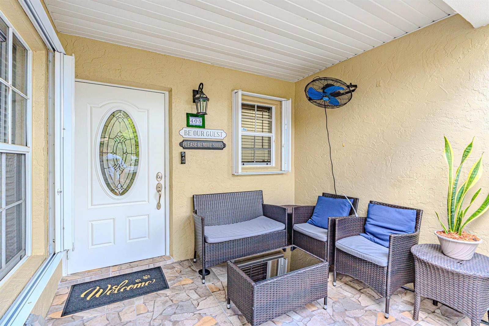 A covered patio features wicker furniture, a glass-topped table, and a white front door — 405 Maplewood Drive # 405, FL 33415, FL