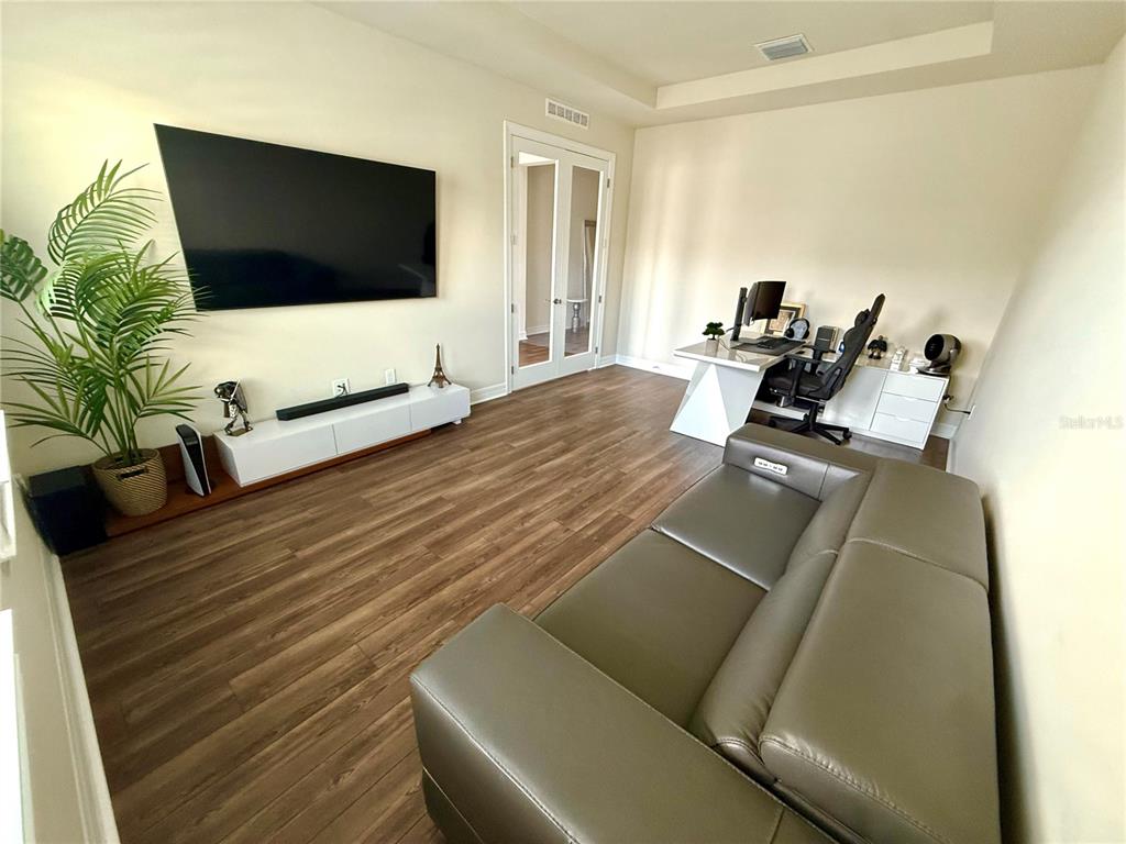 A living room features wood-look flooring, a wall-mounted television, a leather sofa, and a desk — 8441 PARK CLIFF WAY, ORLANDO, FL
