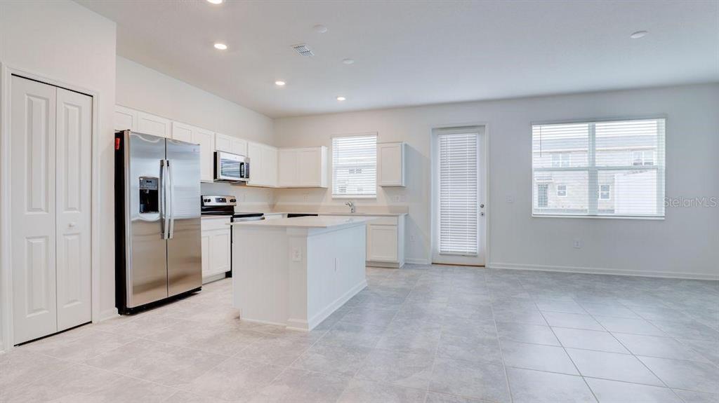 A modern kitchen features white cabinetry, stainless steel appliances, a center island, and tile flooring — 248 NINE IRON DRIVE, DAVENPORT, FL