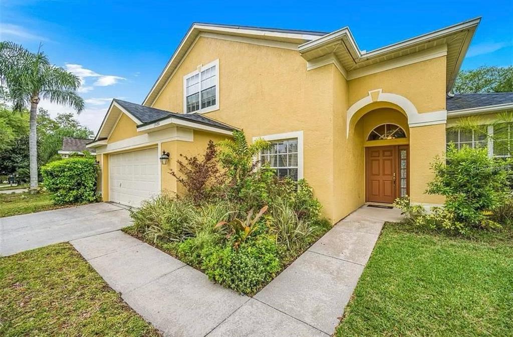 A yellow two-story house with a two-car garage, arched entryway, and a front garden — 19151 DOVE CREEK DRIVE, TAMPA, FL