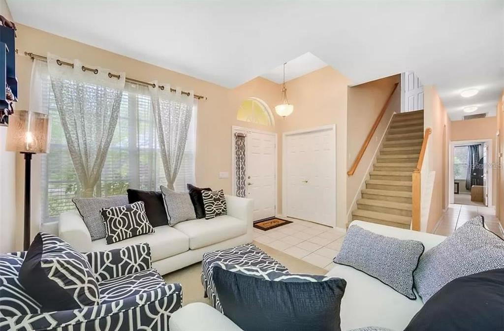 A living room with beige walls, white sofas, patterned pillows, and a staircase — 19151 DOVE CREEK DRIVE, TAMPA, FL