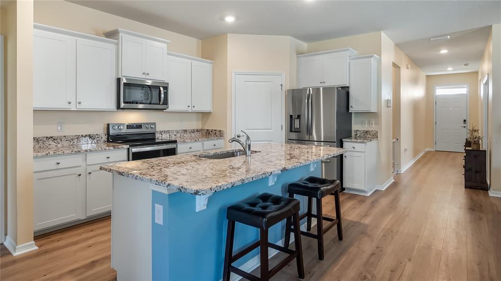 A kitchen features white cabinets, granite countertops, a center island with stools, and stainless appliances — 8033 PENROSE PLACE, WILDWOOD, FL
