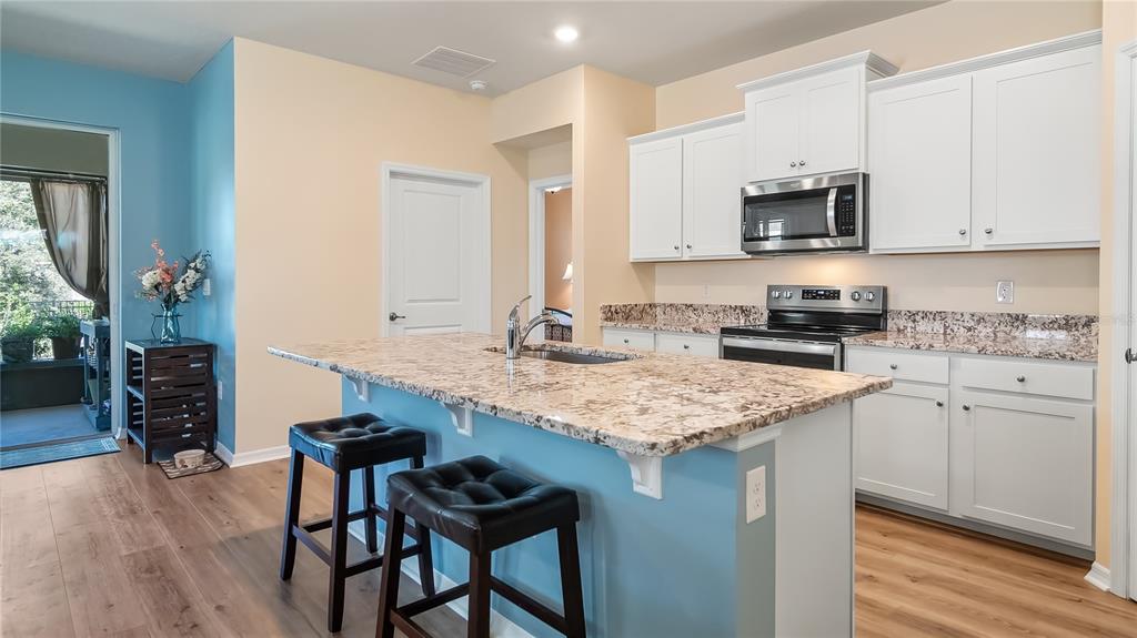 A kitchen with a granite-topped island, white cabinets, stainless steel appliances, and light wood flooring — 8033 PENROSE PLACE, WILDWOOD, FL