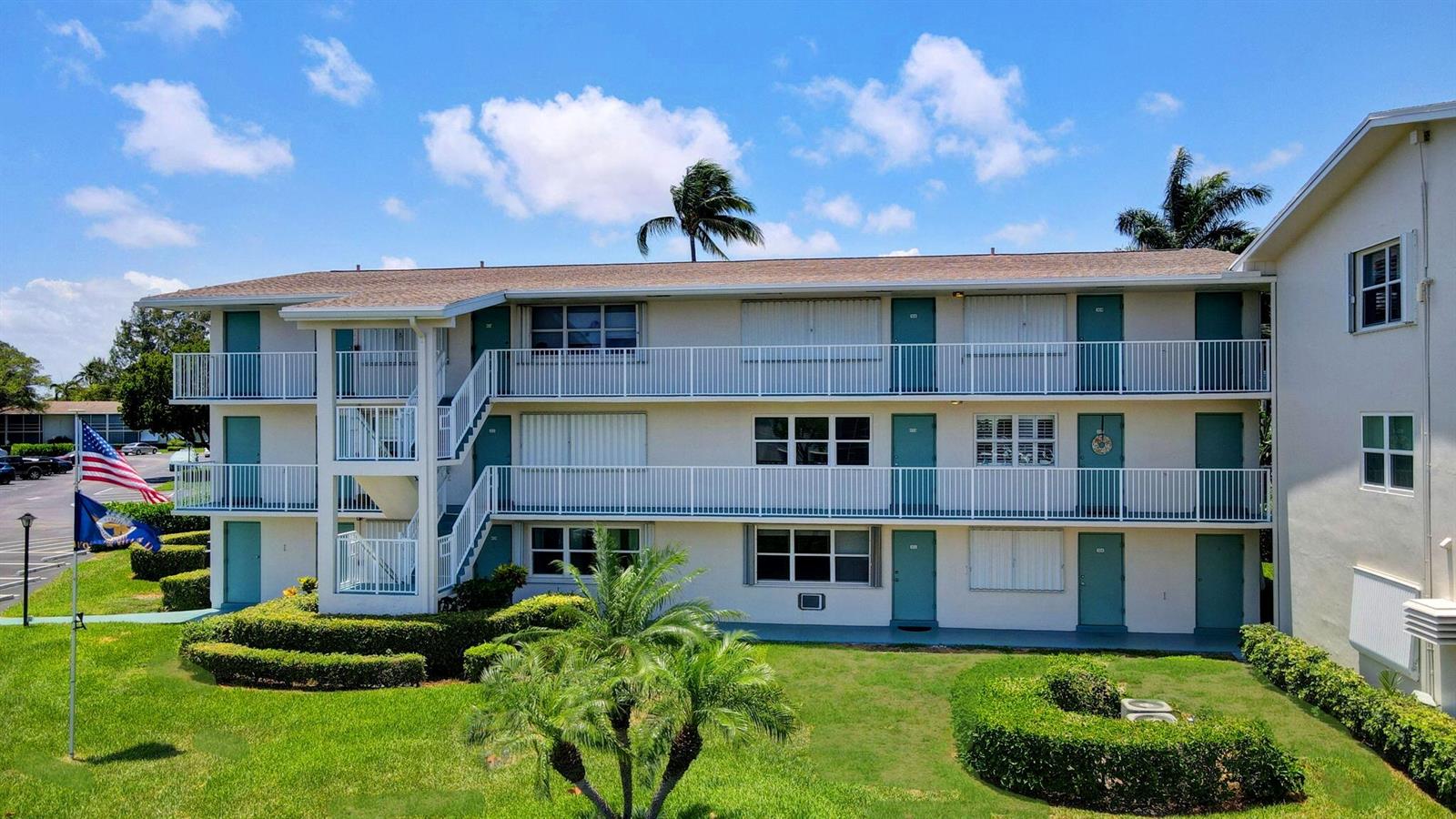 A three-story apartment building with teal doors, white railings, and a landscaped lawn — 210 Horizons E # 103, Boynton Beach FL 33435, BOYNTON BEACH, FL