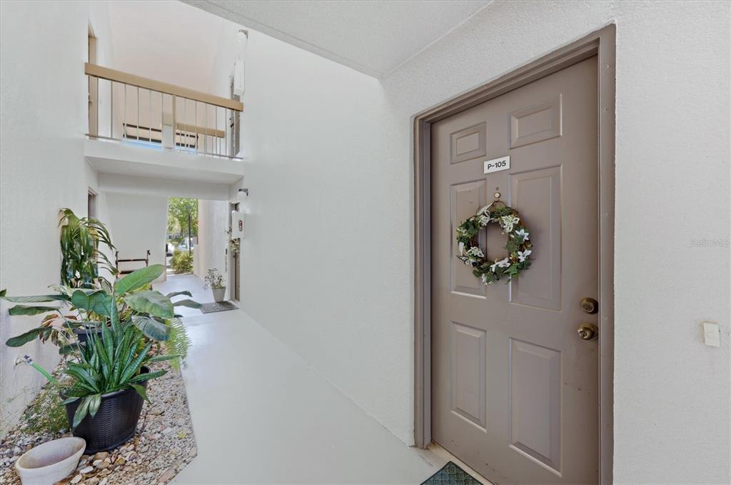 A tan apartment door with a wreath is located in an outdoor hallway with plants — 1515 FORREST NELSON BOULEVARD UNIT P105, PORT CHARLOTTE, FL