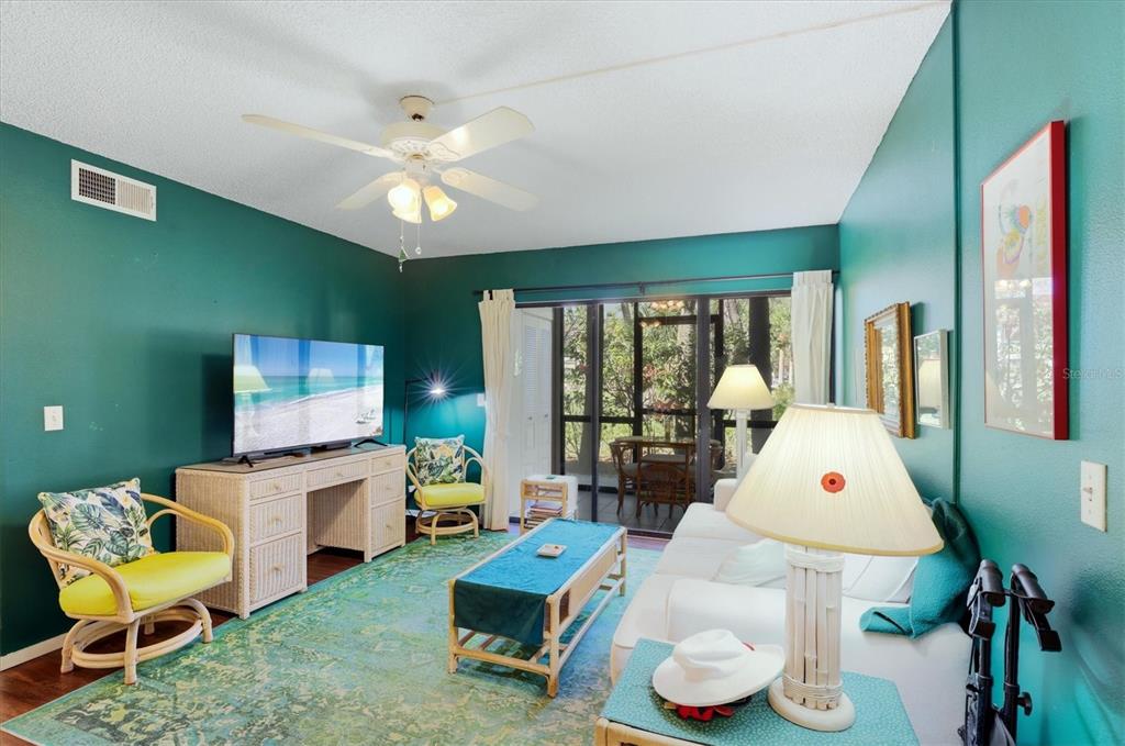 A living room with teal walls, a white sofa, wicker furniture, and a sliding glass door — 1515 FORREST NELSON BOULEVARD UNIT P105, PORT CHARLOTTE, FL