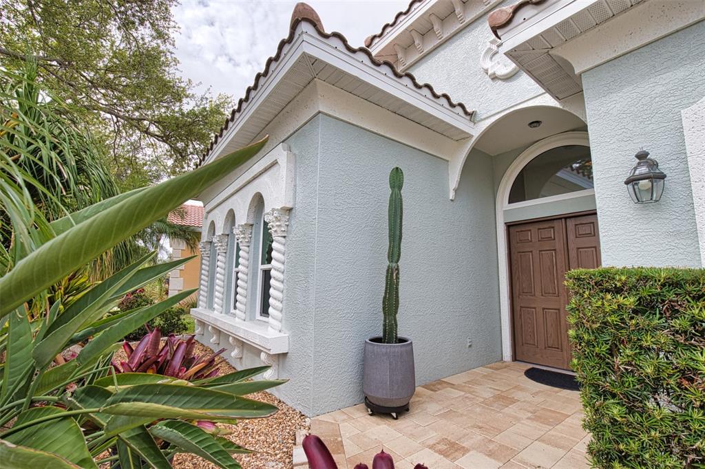 A light blue stucco house exterior with arched windows, a brown door, and a potted cactus — 221 RIO TERRA, VENICE, FL