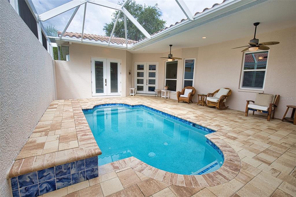 A screened-in patio features a swimming pool, stone pavers, and outdoor seating — 221 RIO TERRA, VENICE, FL
