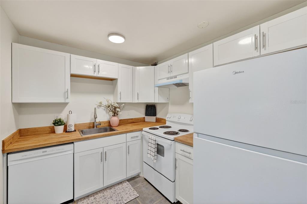 A small kitchen features white cabinets, wood countertops, white appliances, and a stainless steel sink — 11715 RAINTREE VILLAGE BOULEVARD UNIT A, TEMPLE TERRACE, FL