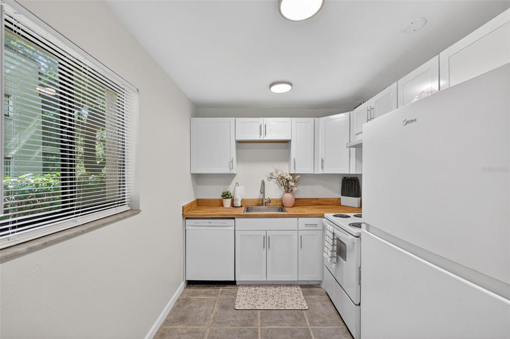 A small kitchen features white cabinets, a wood countertop, a window, and white appliances — 11715 RAINTREE VILLAGE BOULEVARD UNIT A, TEMPLE TERRACE, FL
