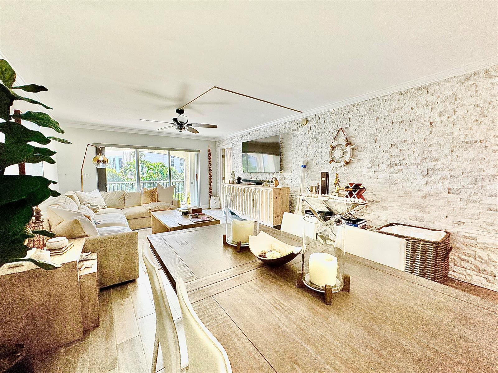 A living and dining room features a stone accent wall, wooden furniture, and balcony access — 2871 N Ocean Boulevard # R248, Boca Raton FL 33431, BOCA RATON, FL