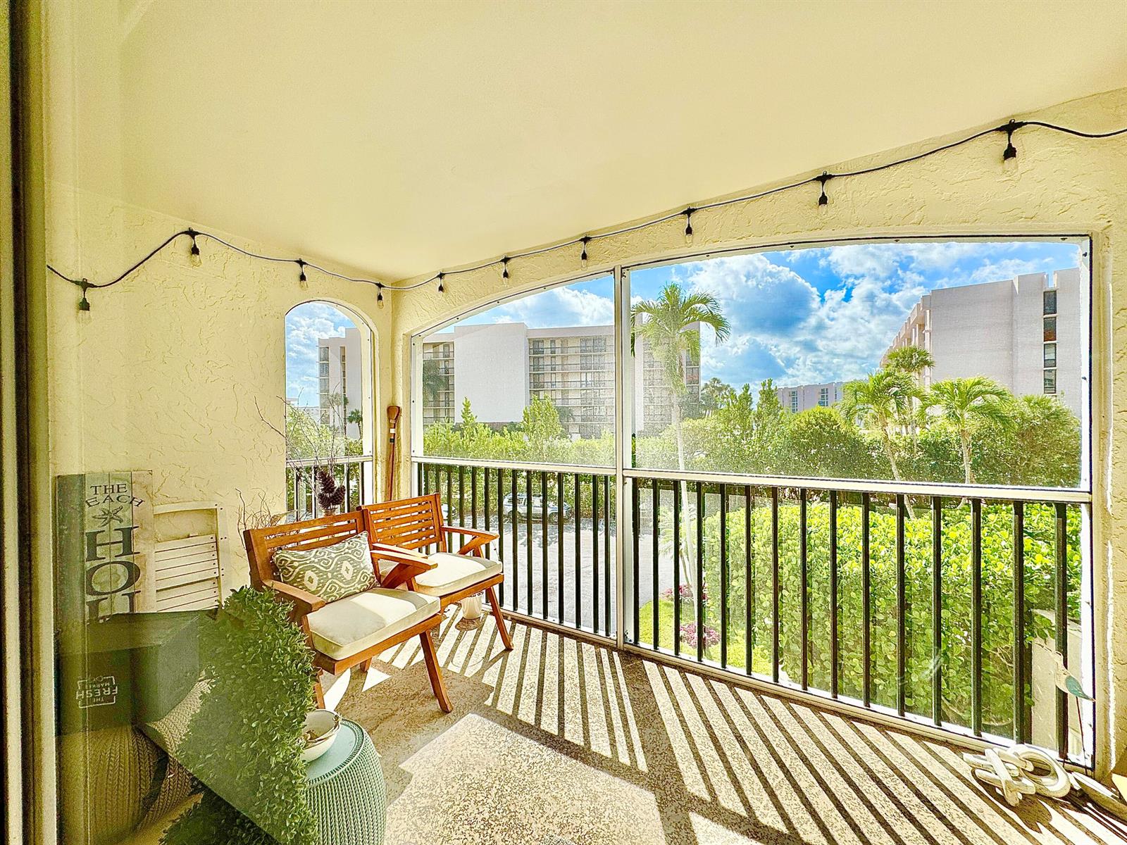 A screened-in balcony features two wooden chairs, string lights, and a view of landscaping — 2871 N Ocean Boulevard # R248, Boca Raton FL 33431, BOCA RATON, FL