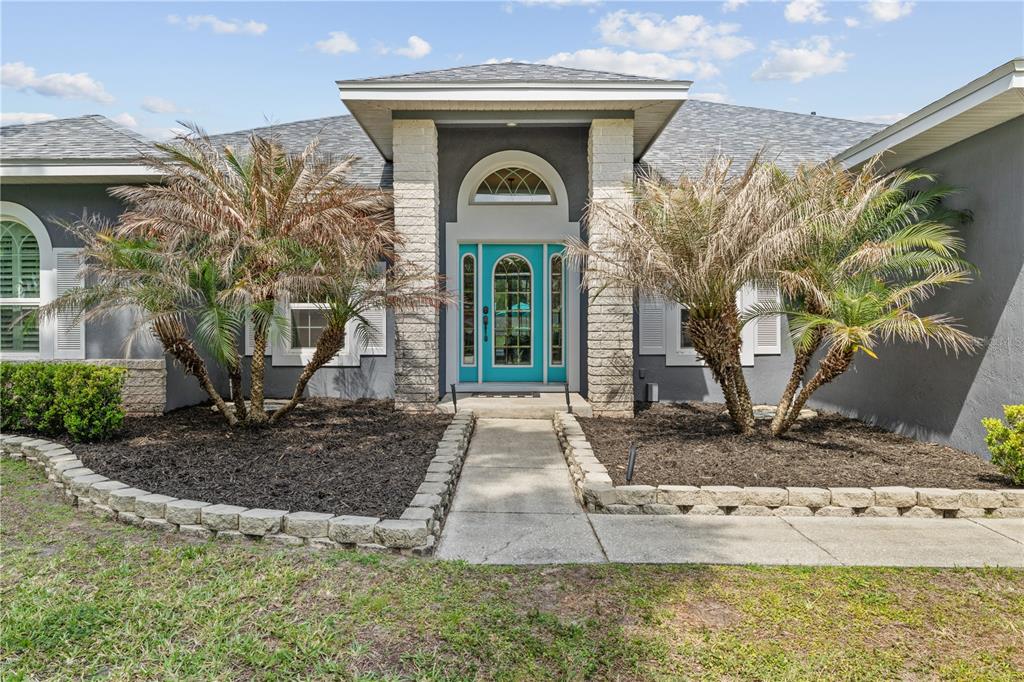 The exterior of a house features a turquoise front door, stone columns, and two palm trees — 1095 W LAKE HAMILTON DRIVE, WINTER HAVEN, FL