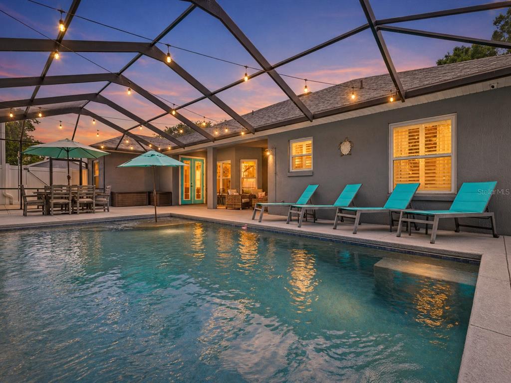A swimming pool with lounge chairs sits under a screened-in patio at dusk — 1095 W LAKE HAMILTON DRIVE, WINTER HAVEN, FL
