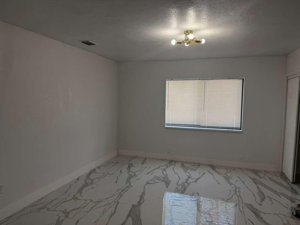 An empty room features white walls, a gold light fixture, and white marble-patterned tile flooring — 160 SE 15th Avenue Unit B, Pompano Beach FL 33060, POMPANO BEACH, FL