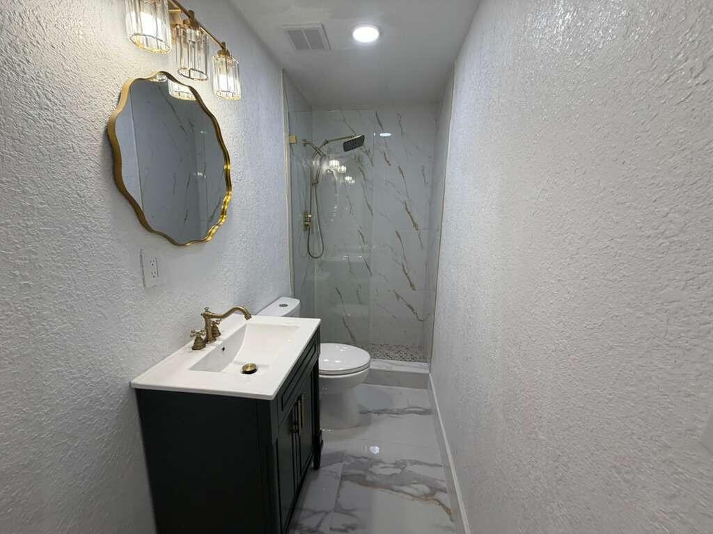 A modern bathroom features a black vanity, gold fixtures, a scalloped mirror, and marble-look tile — 160 SE 15th Avenue Unit B, Pompano Beach FL 33060, POMPANO BEACH, FL