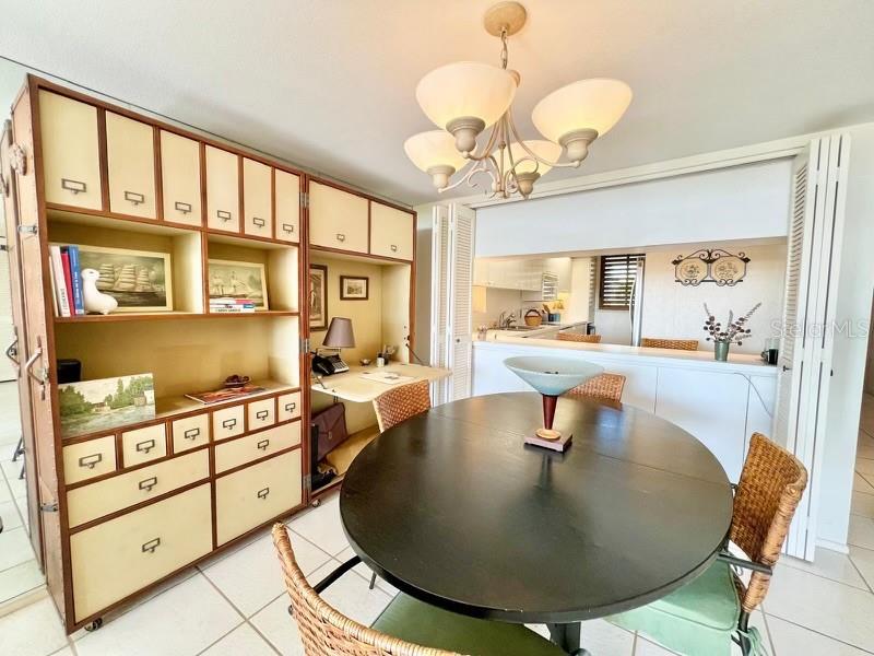 A dining area features a round table, wicker chairs, a large storage unit, and a chandelier — 1065 GULF OF MEXICO DRIVE UNIT 302, LONGBOAT KEY, FL