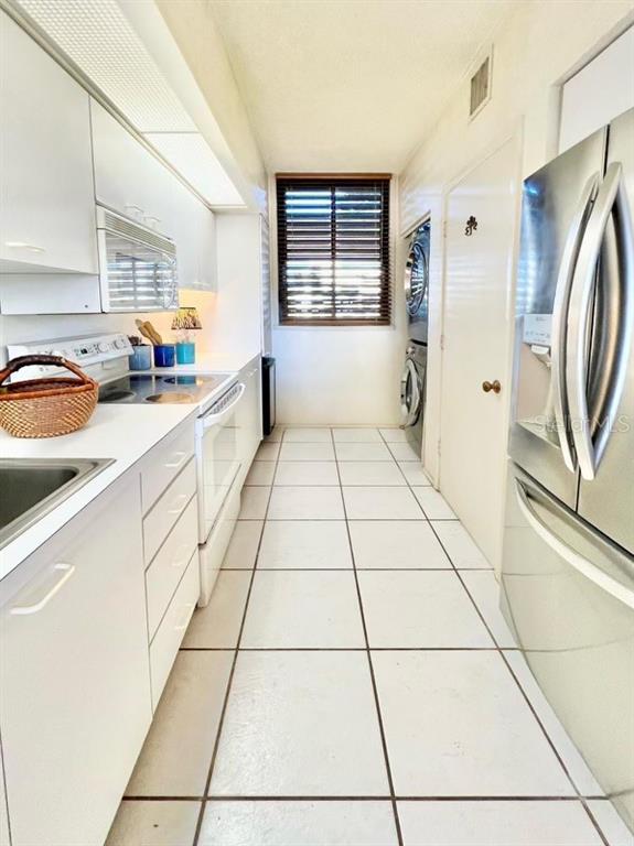 A galley kitchen features white cabinetry, stainless steel appliances, and white tile flooring — 1065 GULF OF MEXICO DRIVE UNIT 302, LONGBOAT KEY, FL