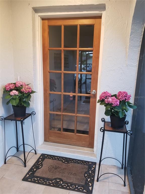 A wooden glass-paneled door is flanked by two potted hydrangea plants on metal stands — 1720 FOSSIL DRIVE, ENGLEWOOD, FL