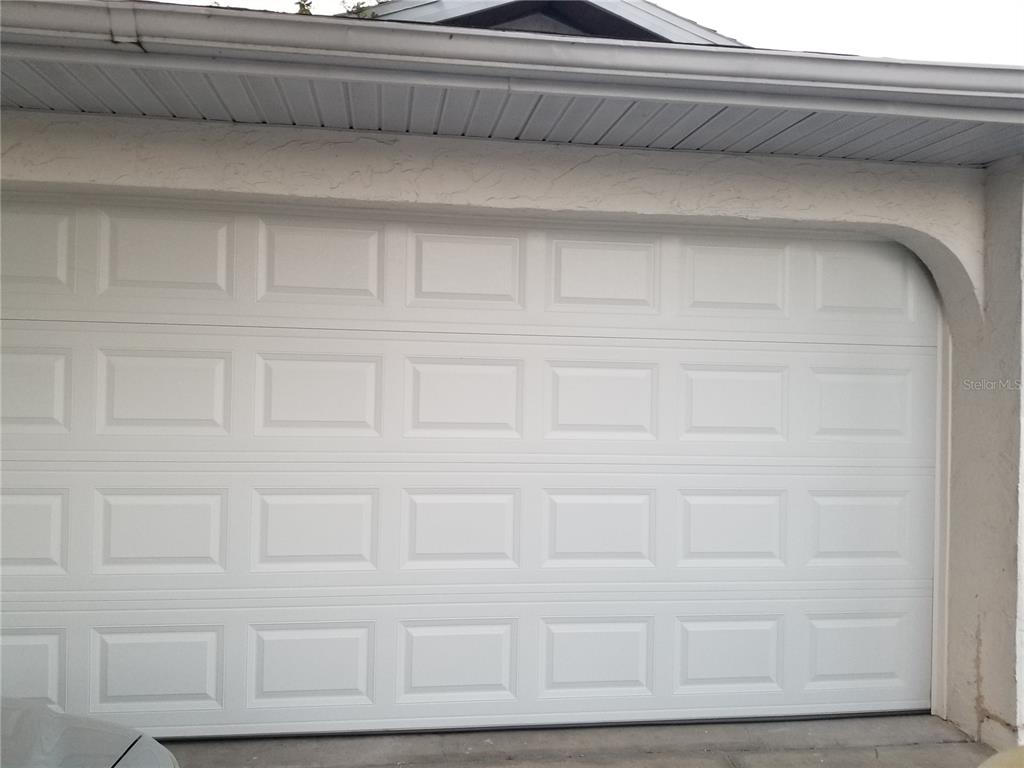 A white, multi-panel garage door is set within a stucco exterior wall — 1720 FOSSIL DRIVE, ENGLEWOOD, FL