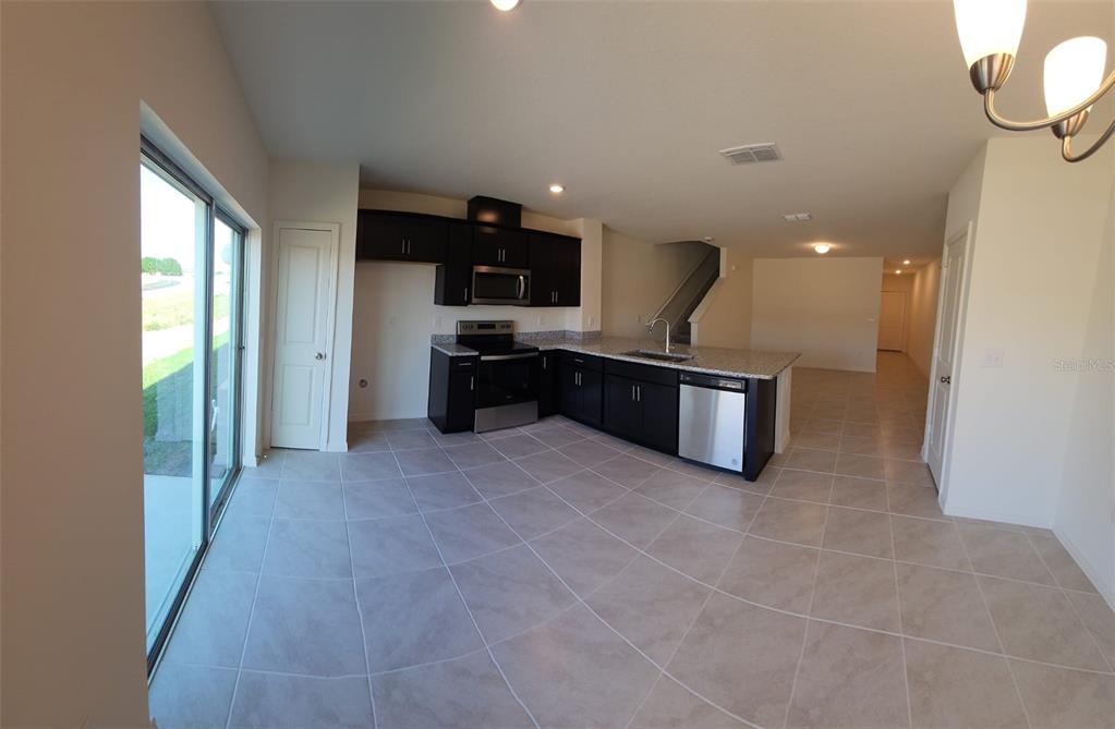A kitchen with dark cabinets, granite countertops, stainless steel appliances, and light tile flooring — 1604 MIRABELLA CIRCLE, DAVENPORT, FL