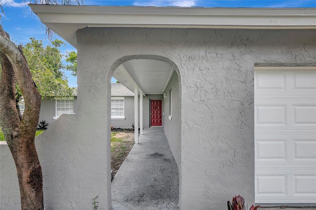 A gray stucco house exterior features a covered walkway leading to a red front door — 917 WINCHESTER COURT, BRANDON, FL