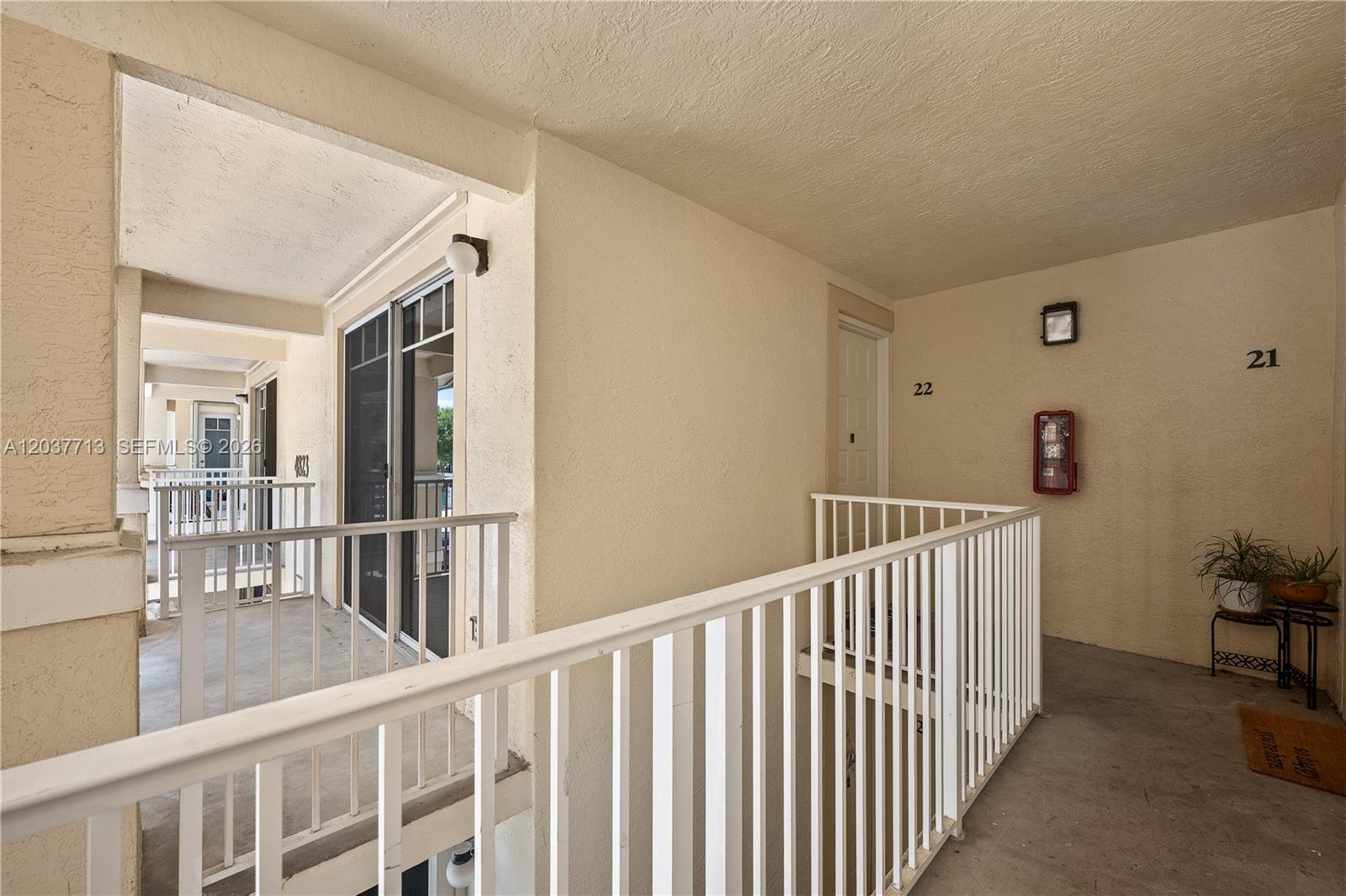 An outdoor apartment building walkway features white railings, unit numbers, and a red fire extinguisher — 4823 Chancellor Dr # 22, Jupiter FL 33458, JUPITER, FL