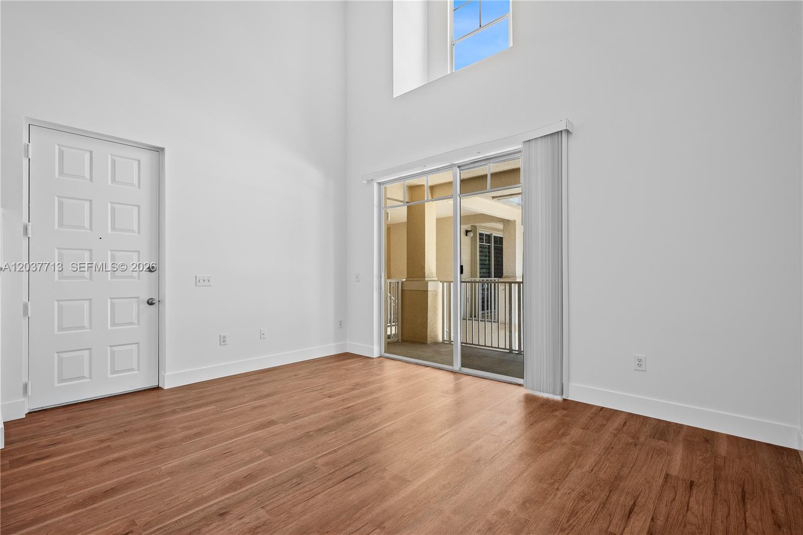 A room with high ceilings, wood-look flooring, a white door, and a sliding glass door — 4823 Chancellor Dr # 22, Jupiter FL 33458, JUPITER, FL