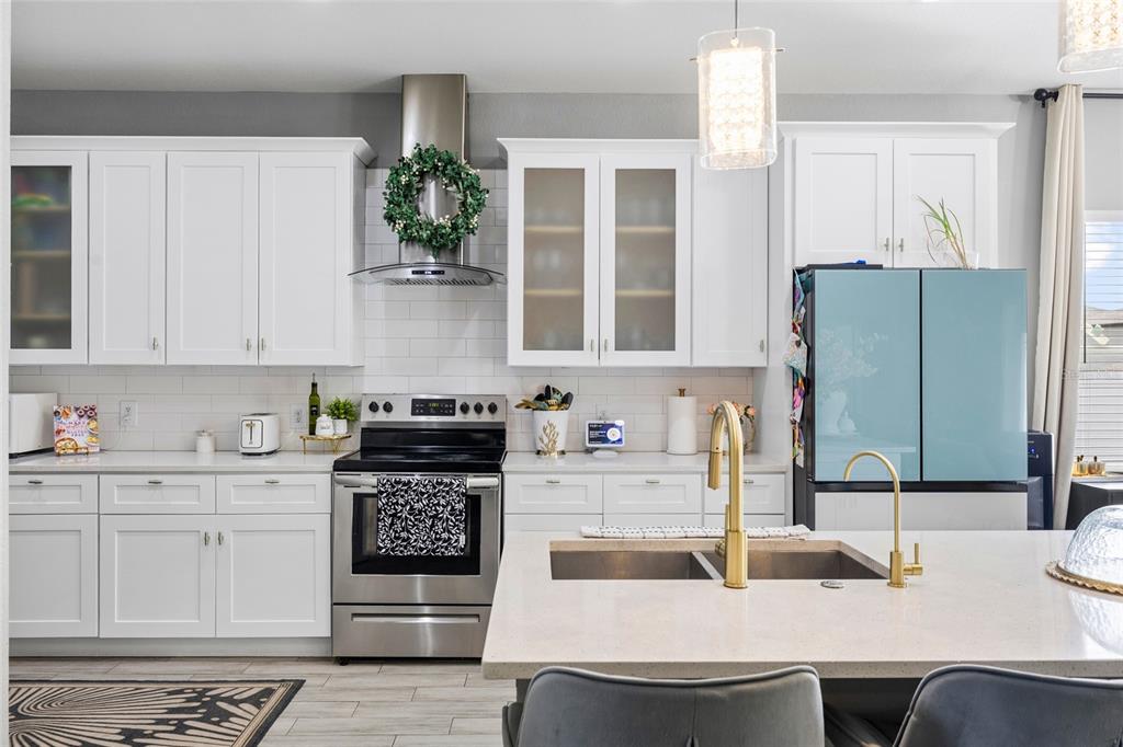 A modern kitchen features white cabinets, stainless steel appliances, a quartz island, and gold fixtures — 10917 DUNSCORE COTTAGE WAY, WIMAUMA, FL