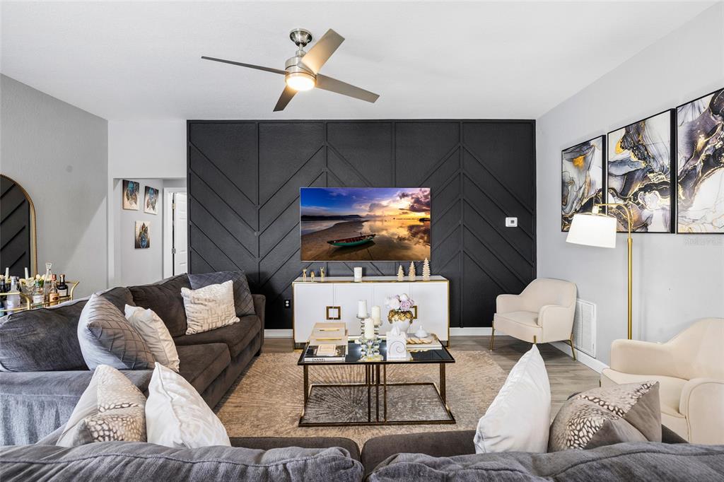A living room features a dark accent wall with geometric molding, a television, and gray sofas — 10917 DUNSCORE COTTAGE WAY, WIMAUMA, FL