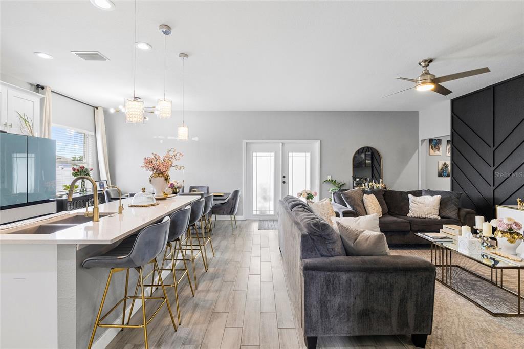 An open-concept kitchen and living area features a breakfast bar, gray sofa, and tile flooring — 10917 DUNSCORE COTTAGE WAY, WIMAUMA, FL