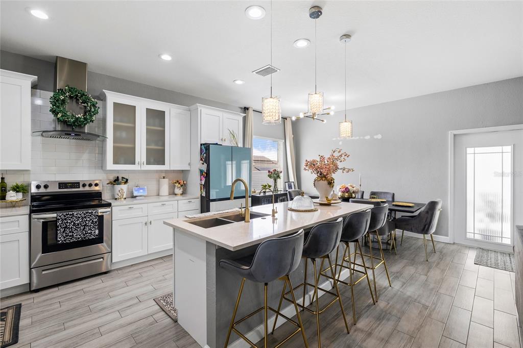 A modern kitchen features white cabinetry, a large island with bar seating, and stainless appliances — 10917 DUNSCORE COTTAGE WAY, WIMAUMA, FL