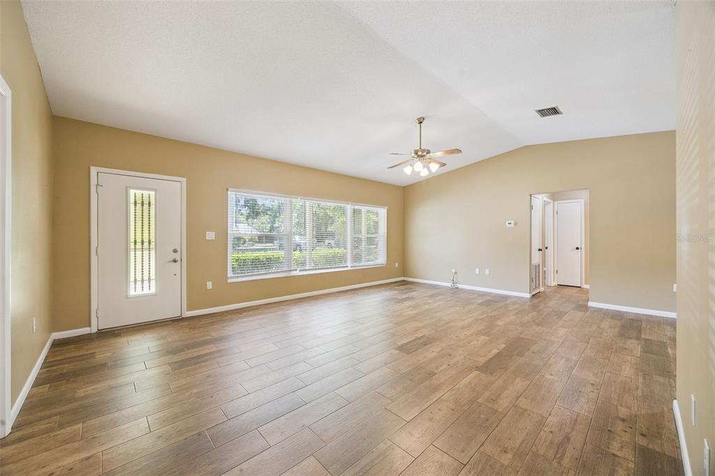 A living room with wood-look tile flooring, a vaulted ceiling, and a large front window — 80 WHITCOMB AVENUE, UMATILLA, FL