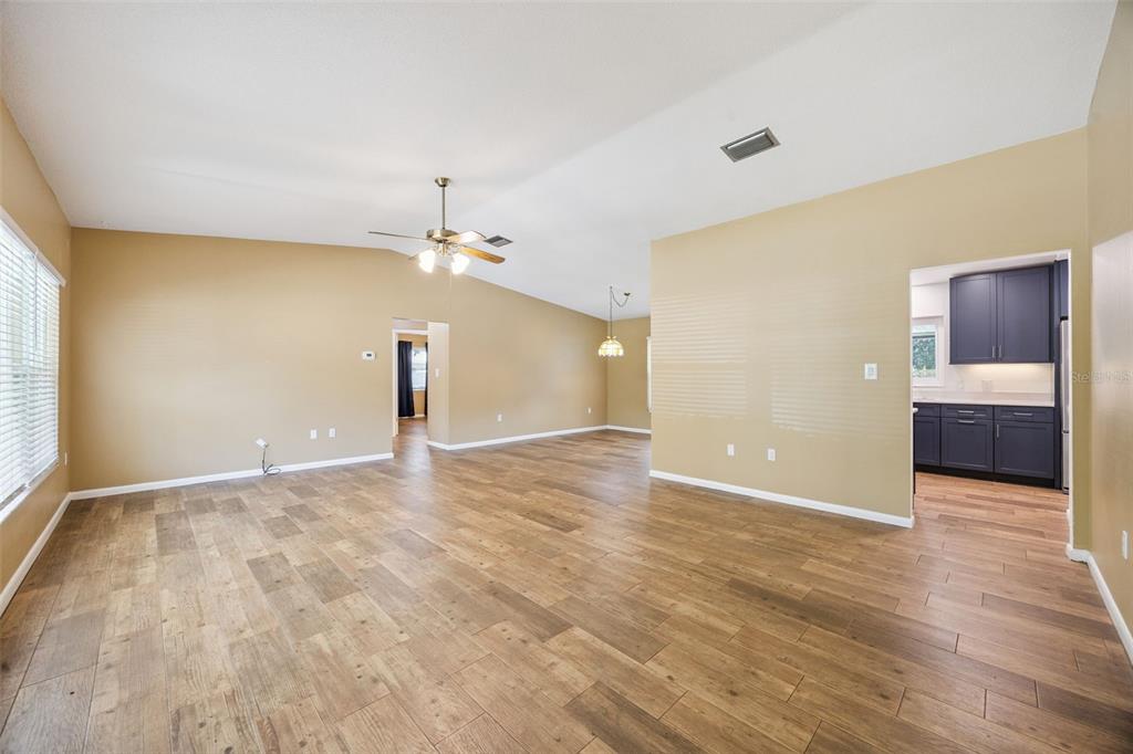 An open-concept living area with wood-look flooring, vaulted ceilings, and a view into the kitchen — 80 WHITCOMB AVENUE, UMATILLA, FL