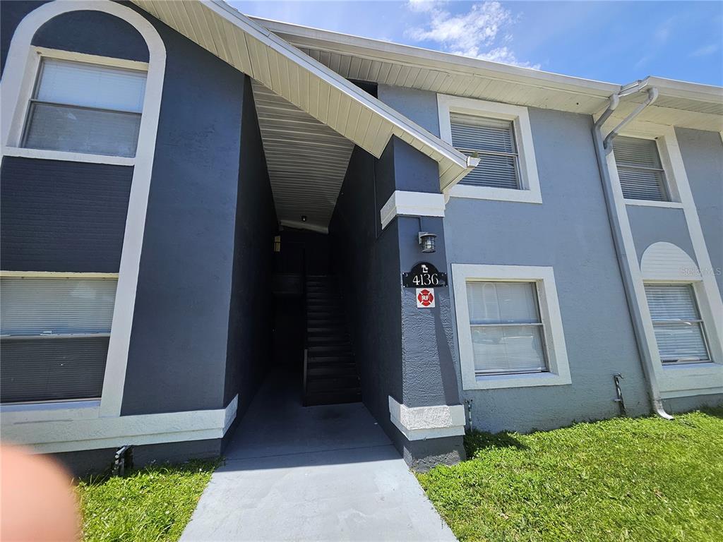A two-story apartment building exterior features gray stucco walls, white trim, and a recessed staircase — 4136 PERSHING POINTE PLACE UNIT 4, ORLANDO, FL
