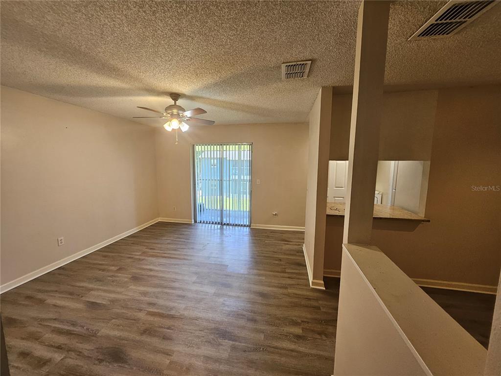 An open living area features wood-look flooring, a ceiling fan, and sliding glass patio doors — 4136 PERSHING POINTE PLACE UNIT 4, ORLANDO, FL