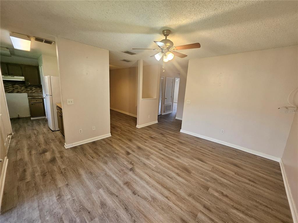 A living room with wood-look flooring leads to a kitchen and a hallway — 4136 PERSHING POINTE PLACE UNIT 4, ORLANDO, FL